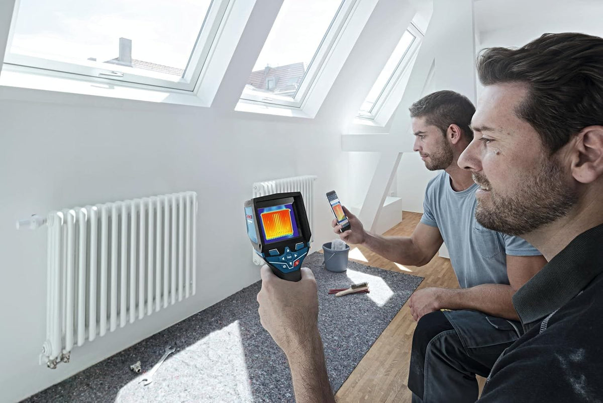 Two professionals inspecting a radiator, with one using the thermal camera and the other viewing the real-time thermal image on a connected smartphone