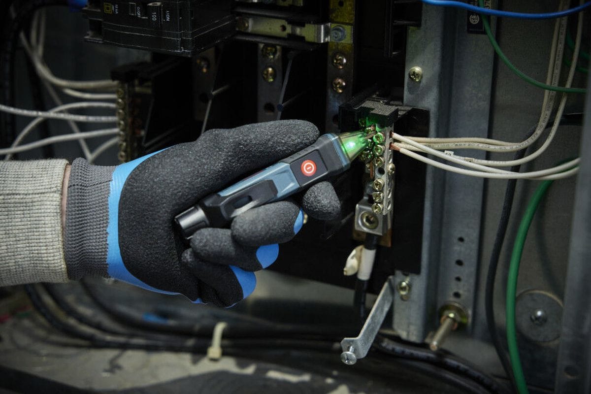 A real-world maintenance application showing a gloved technician using the Bosch GVD1000-15 circuit detector stick to inspect a neutral grounding bus terminal block inside an electrical panel box. The transparent indicator tip glows green, verifying a safe, de-energized connection before running structural repairs.