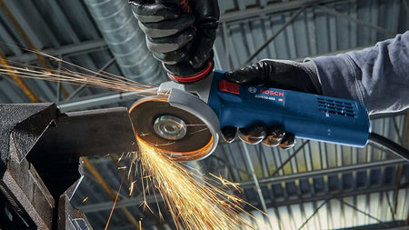 A close-up action shot of a worker using the grinder on metal, creating a stream of orange sparks.