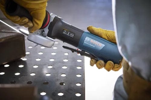An action photo showing a person in work gloves operating the corded angle grinder on a metal workbench, highlighting the large no lock-on paddle switch on the underside of the tool.