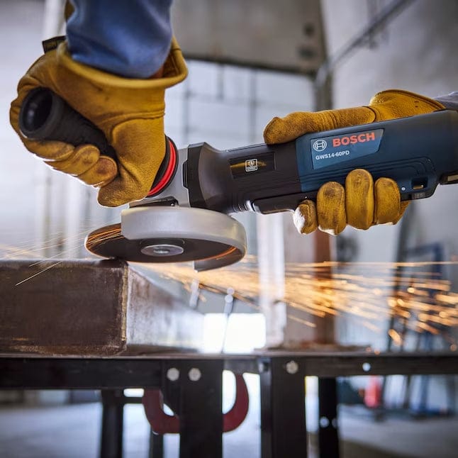 A close-up action view of an operator in yellow work gloves using the Bosch GWS14-60PD angle grinder to cut through a metal beam, producing a large spray of orange sparks.
