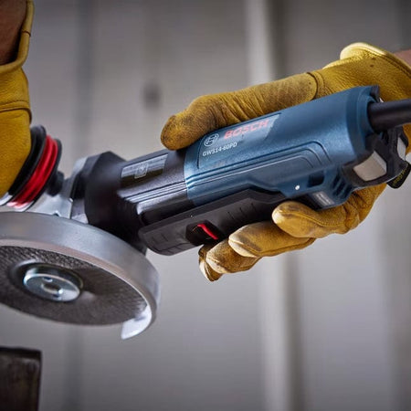 An operator's hands shown wearing yellow protective gloves and holding the Bosch GWS14-60PD grinder, demonstrating the use of the no lock-on paddle switch for controlled operation.