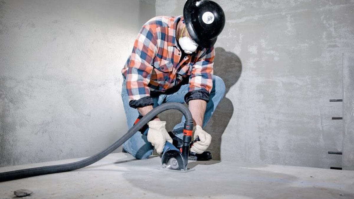 An operator wearing protective gear while using the Bosch GWS18V-13C angle grinder for concrete slab cutting, demonstrating the effective use of a HEPA-compliant dust collection system.