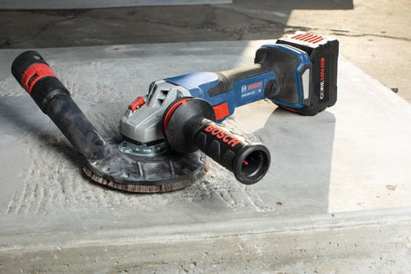The Bosch PROFACTOR 18V angle grinder fitted with a professional surface grinding shroud and a diamond cup wheel, shown resting on a concrete surface prepared for industrial finishing.