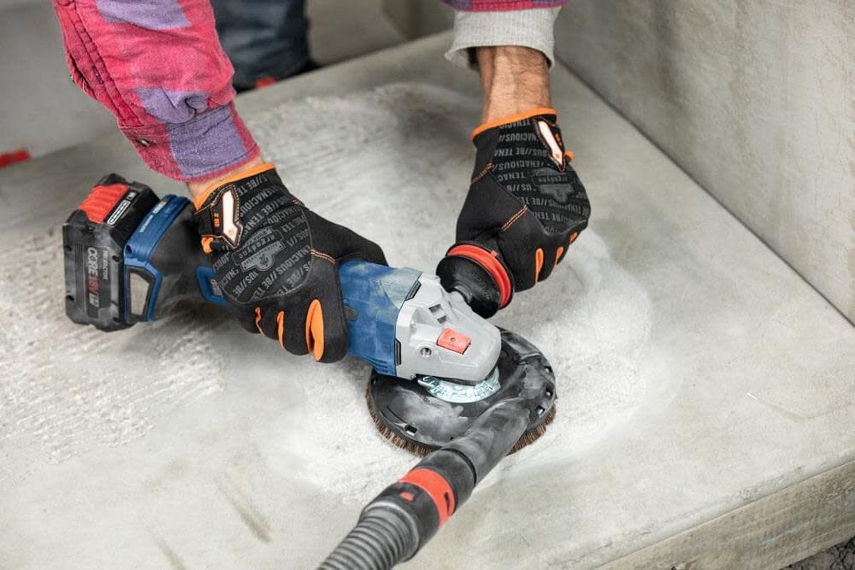 A contractor utilizing the Bosch 18V brushless grinder with a surface grinding attachment to smooth concrete, illustrating the tool's power and the high-efficiency dust management capabilities of the PROFACTOR system.