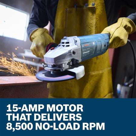 An action close-up showing a workshop fabricator wearing bright yellow leather safety welding gloves and a matching heavy leather apron operating the Bosch 15-Amp metal angle grinder. The tradesman applies steady mechanical pressure to grind down a thick steel frame bar workpiece on a table setup, set above a lower marketing text banner reading 15-Amp motor that delivers 8,500 no-load RPM.