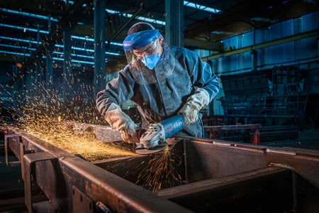 An uncropped workshop view identical to file GWS25-180PR 4.webp, capturing a professional welder smoothing out a metal union seam with the Bosch GWS25-180PR 7-inch angle grinder. This variant features no text blocks, providing a clear perspective of the tool's vibration control side grip and adjustable guard positions under ambient body shop lighting.