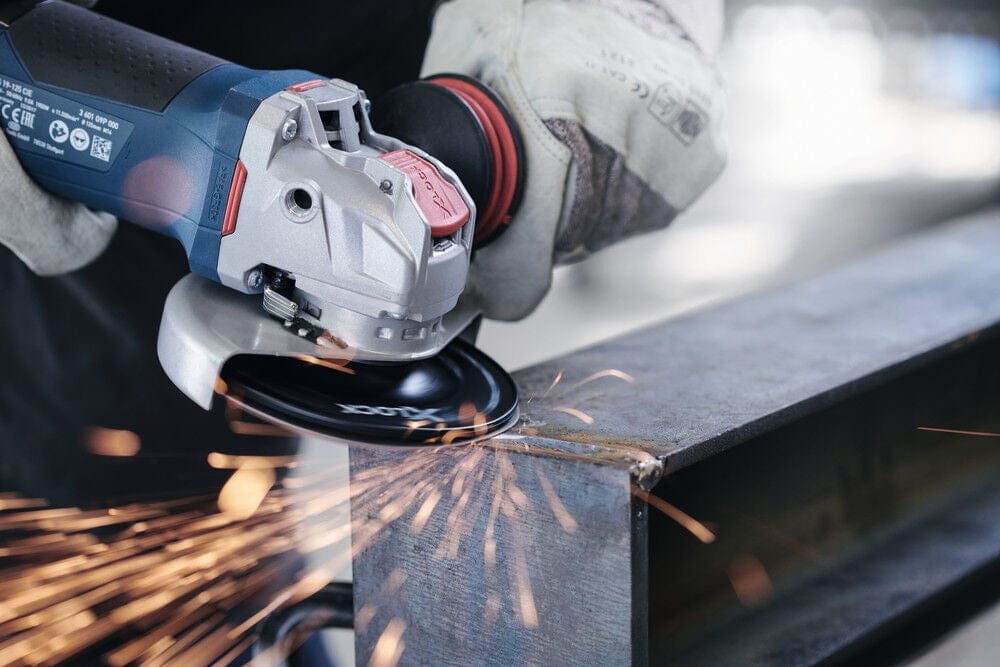 Professional using the Bosch angle grinder to trim the edge of a thick steel structural component on an industrial workbench.