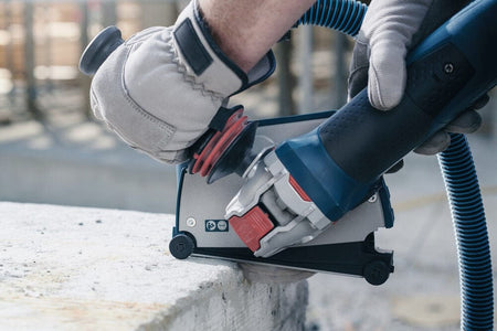 Detailed view of the Bosch angle grinder with a dust extraction guard being used for clean, controlled cutting into a flat concrete slab.