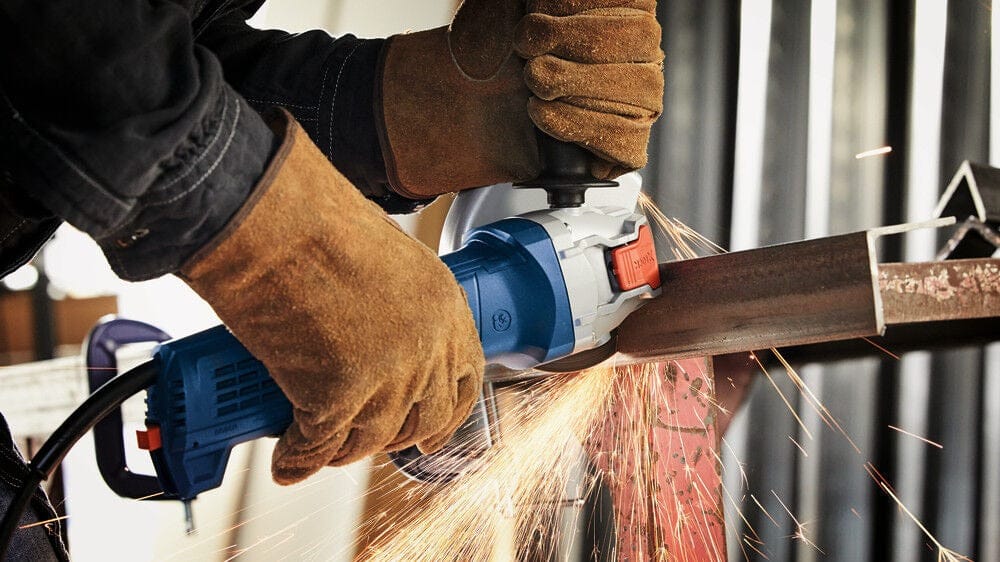 Professional in leather safety gloves using the Bosch 4-1/2 inch angle grinder to cut through a thick metal structural beam, creating sparks.