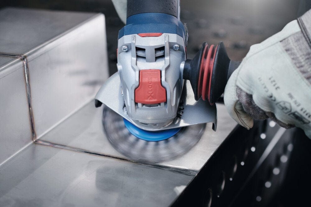 Close-up action shot of the Bosch X-LOCK angle grinder using a wire cup brush to clean a weld bead on a stainless steel surface.