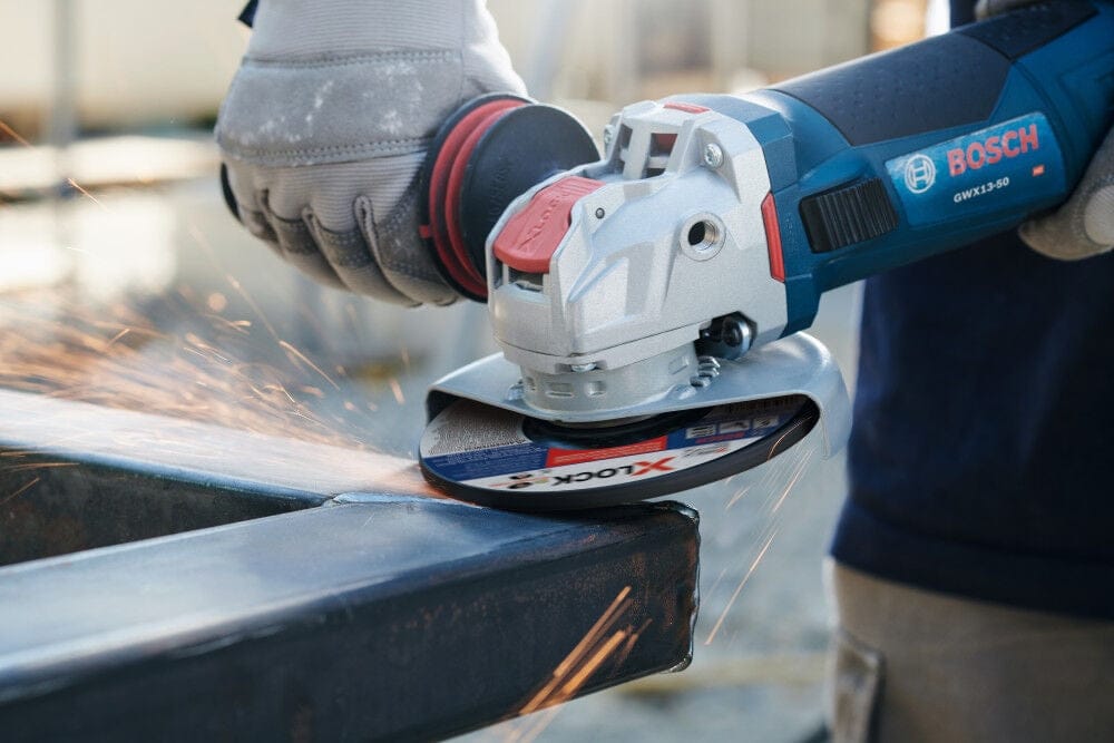 Industrial worker using the Bosch 4-1/2 inch angle grinder for surface grinding on a metal frame, producing sparks on a job site.