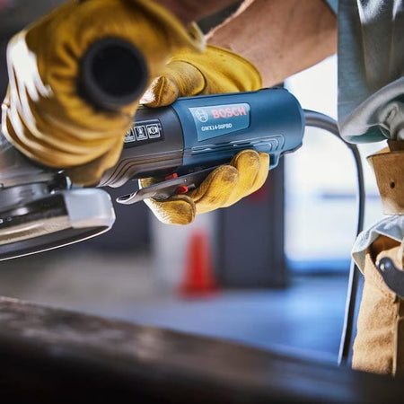 Close-up action shot of an operator in yellow protective work gloves using the Bosch GWX14-50PBD-RT X-LOCK angle grinder for a metal finishing application.