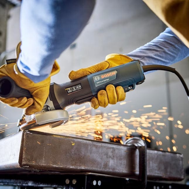 Action view of an operator using the Bosch 5-inch X-LOCK angle grinder to cut through a thick metal workpiece, producing bright orange sparks.
