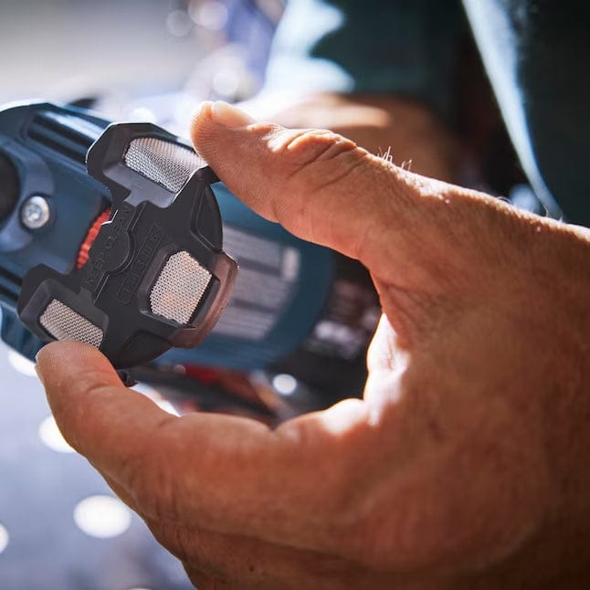Close-up of a person's hands wearing yellow gloves holding a black mesh dust filter near the rear air intake of the Bosch corded angle grinder.