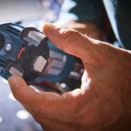 Close-up of a person's hands wearing yellow gloves holding a black mesh dust filter near the rear air intake of the Bosch corded angle grinder.