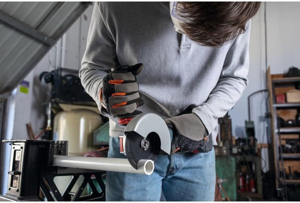 Person cutting white PVC pipe with handheld power tool; pipe secured in vise on workbench in garage setting.