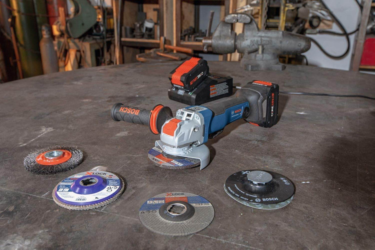Bosch cordless angle grinder on workbench surrounded by five X-LOCK grinding and cutting discs; extra battery visible.