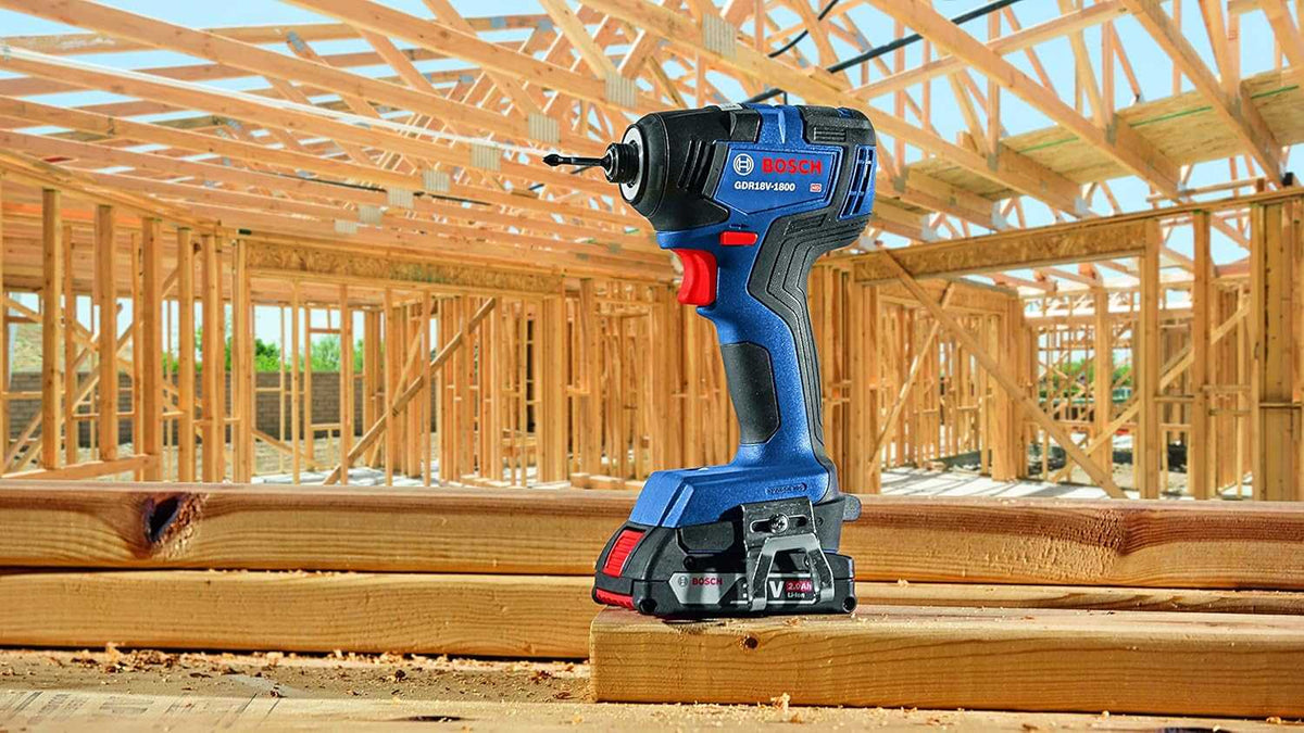 The Bosch GDR18V-1800 18V brushless 1/4 inch hex impact driver equipped with a Phillips bit, standing confidently on a wooden crossbeam at an active residential framing and construction site.