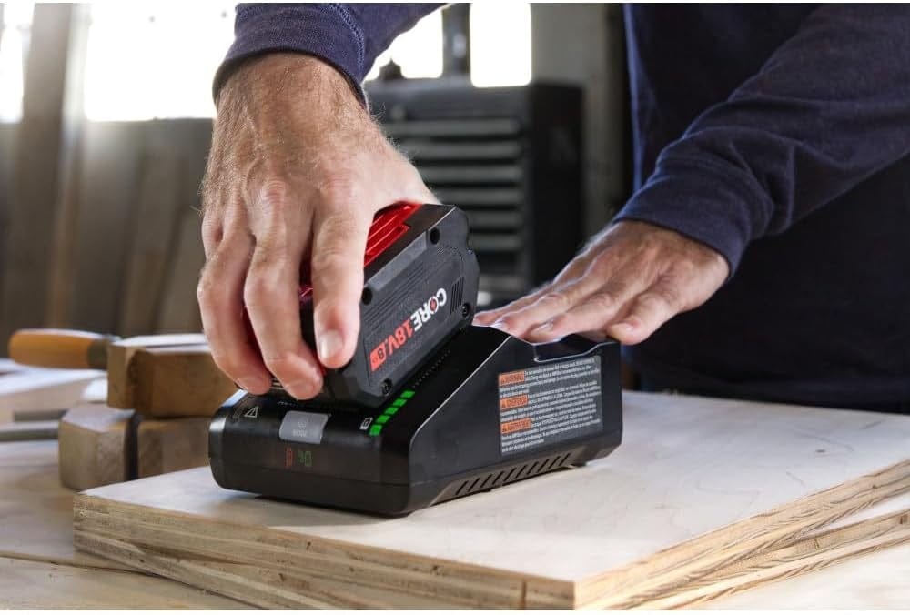 A close-up shot of a person sliding a CORE18V 8.0 Ah high-power battery onto the 16 Amp turbo fast charger on a workshop table.