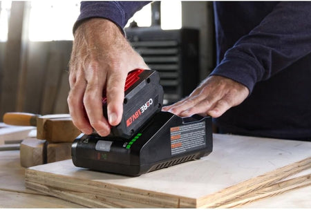 A close-up shot of a person sliding a CORE18V 8.0 Ah high-power battery onto the 16 Amp turbo fast charger on a workshop table.