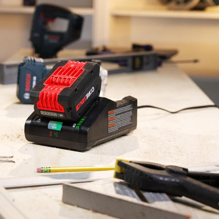 A Bosch CORE18V 8.0 Ah battery charging on the turbo fast charger on a workbench, with hand tools and power tools visible in the blurred background.