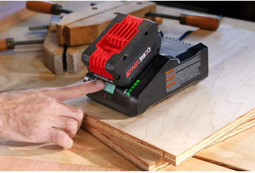 Action shot showing a technician’s hand pressing the green illuminated mode button on the turbo charger while a high-power 8.0 Ah battery is docked on a wooden surface.