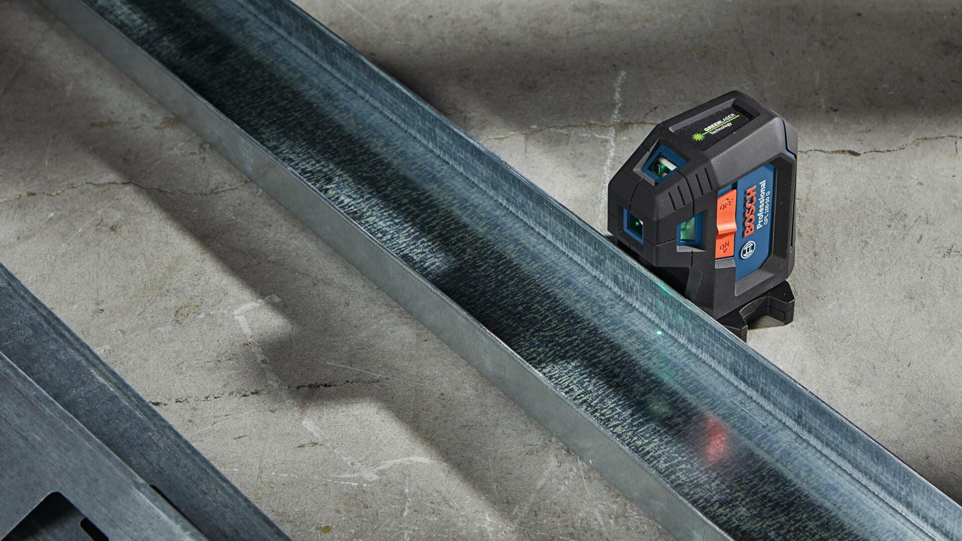Action shot showing the Bosch GPL100-50G laser sitting on the ground, projecting the green level line along a steel stud floor track for construction layout