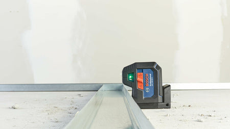 Action shot showing the Bosch GPL100-50G laser set on the floor track, using the green laser dot to verify the alignment of metal studs in a room