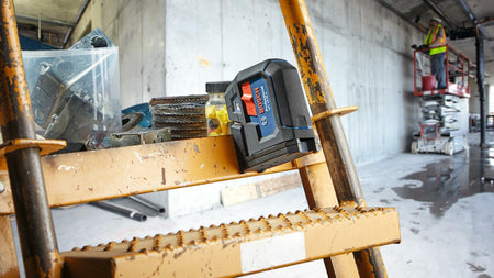 Action shot showing the Bosch GPL100-50G laser magnetically attached to a metal staircase railing, demonstrating the versatility of the integrated multipurpose mount