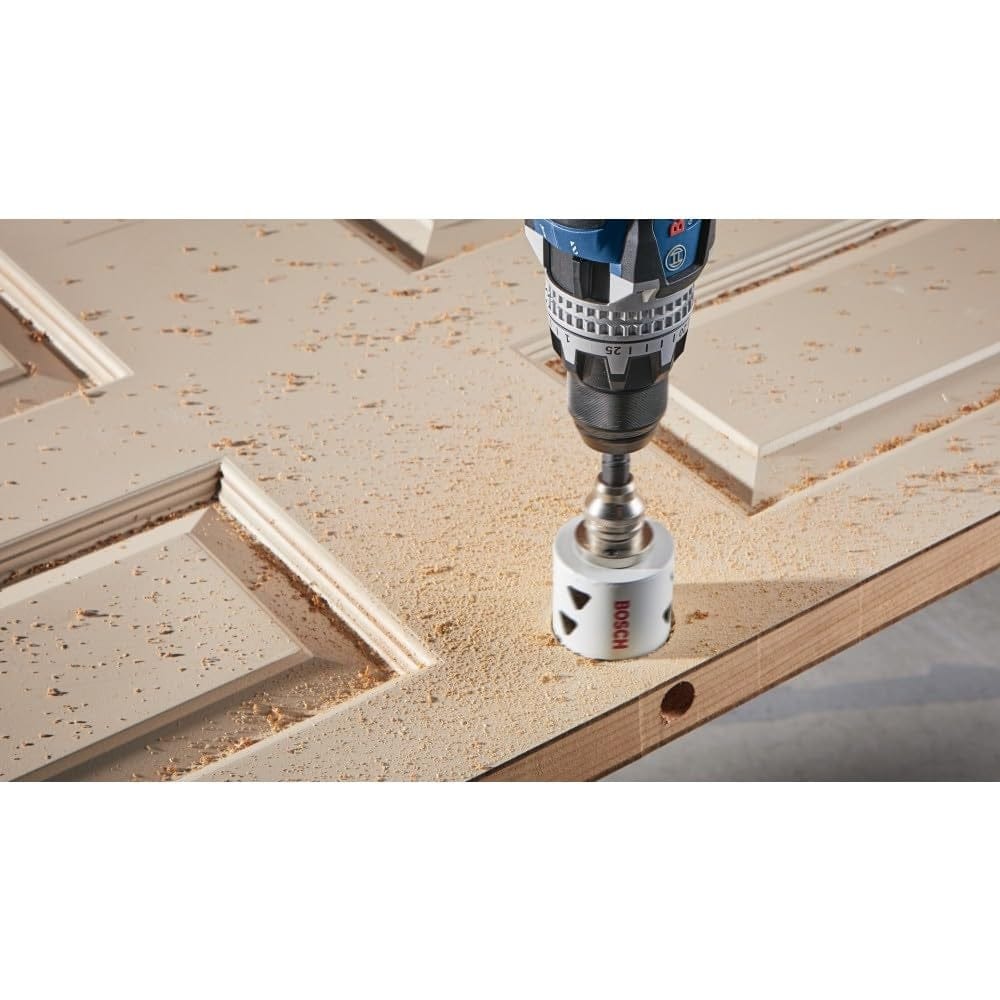 Overhead action shot of a cordless drill with the hole saw cutting a hole into a beige wooden door panel.