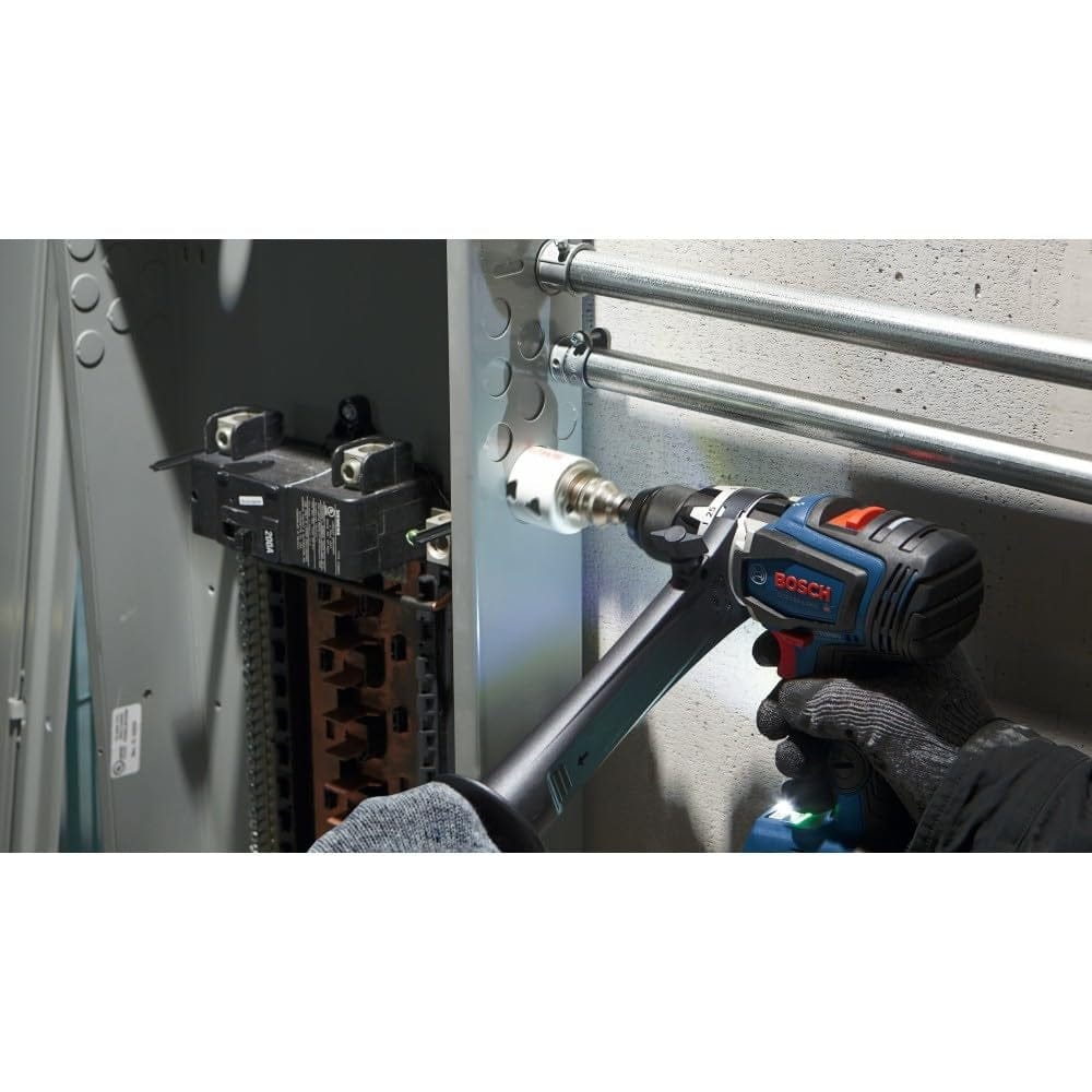 A worker uses a Bosch drill and the hole saw to cut through the side of a grey metal electrical panel box.