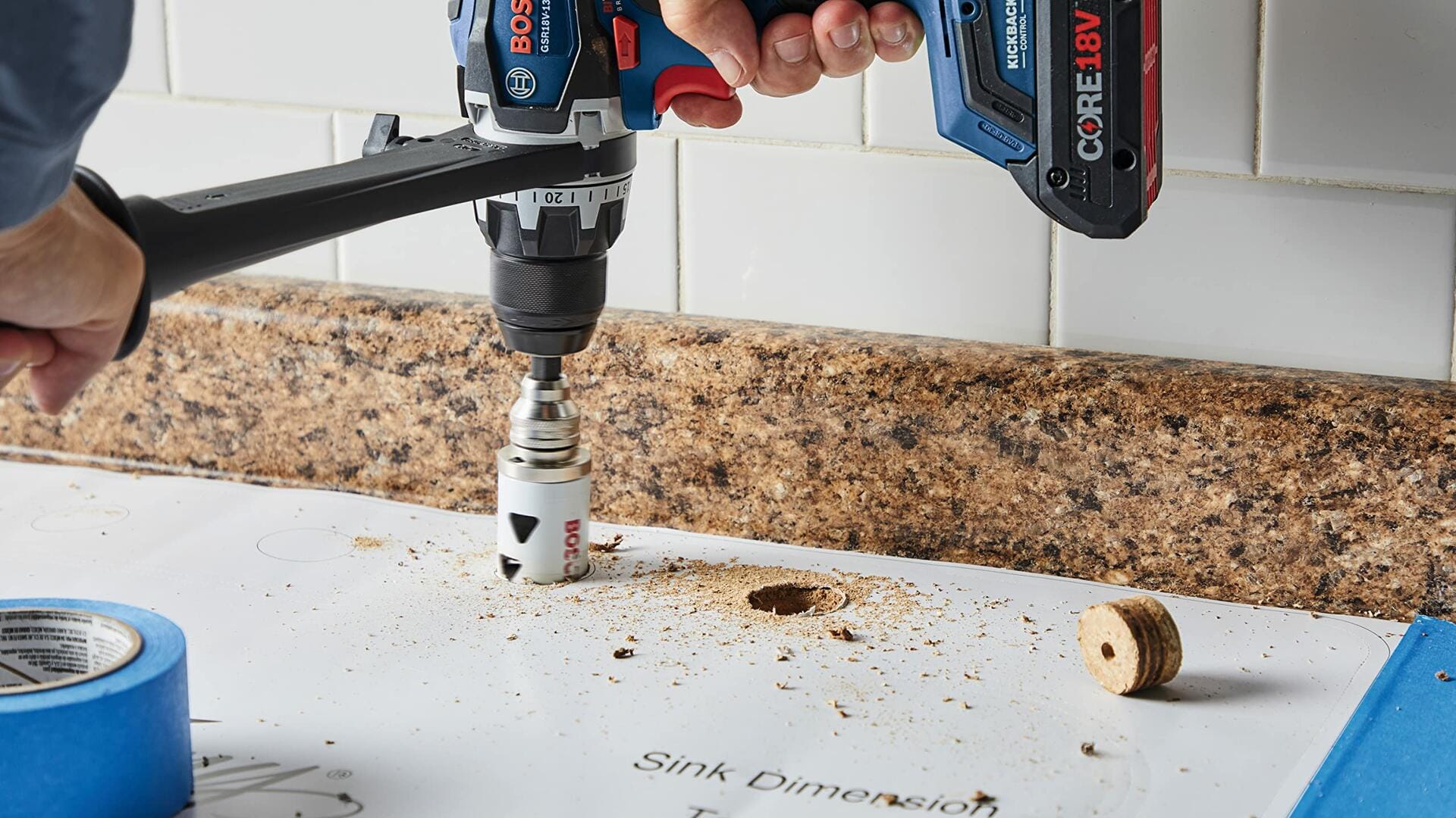 A person uses a Bosch drill with a white bi-metal hole saw to drill a hole through a white laminate countertop, with the wood plug resting nearby.