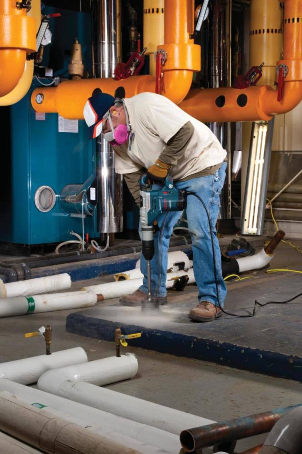 Action shot of a worker in an industrial setting using a large blue Bosch rotary hammer equipped with a core bit and centering pin to drill into a concrete floor.