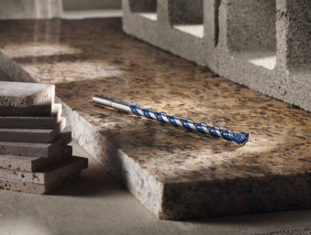 The Bosch 3/8-inch x 10-inch BlueGranite Turbo bit resting on a granite countertop next to a stack of tiles and a concrete block.
