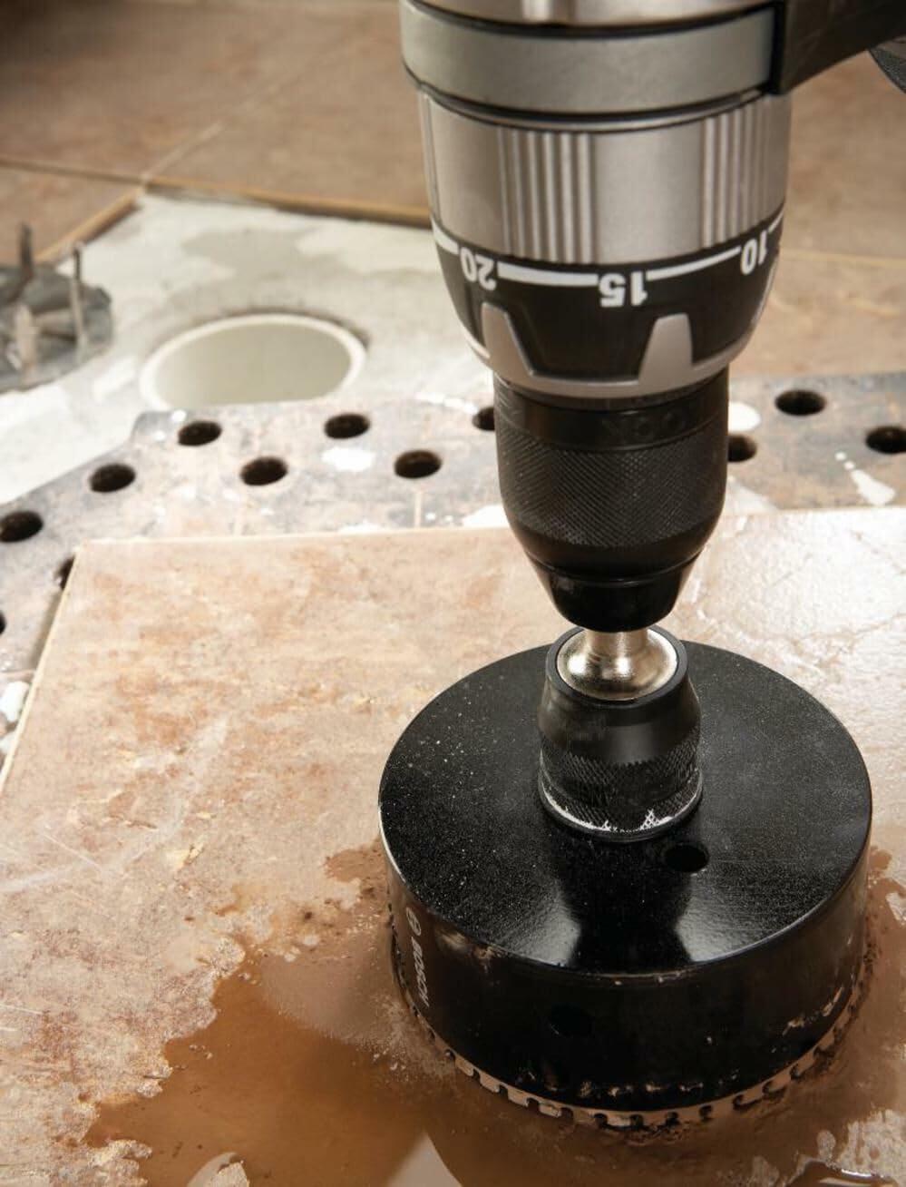 A close-up view of a large Bosch diamond hole saw mounted in a drill, actively cutting a clean hole through a porcelain tile during a wet-cutting process.