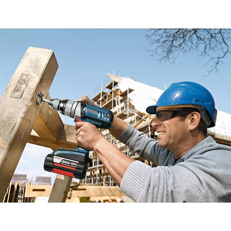 Individual using Bosch 36V cordless drill on large wooden beam; scaffolding and building structure in background.