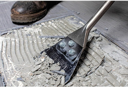 A detailed close-up of the 5-inch Bosch scraper blade removing heavy mortar and floor adhesive, illustrating the high-impact demolition power provided by the SDS-plus hammer attachment.