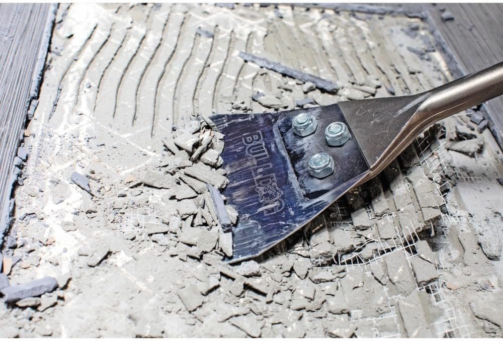 A secondary application shot showing the Bosch HS1418 scraper clearing debris and tile fragments, highlighting the clean removal path created by the professional-grade steel blade.