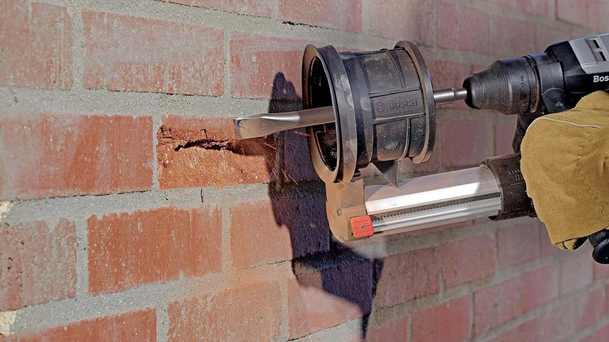 Worker operating a Bosch rotary hammer drill equipped with a dust collector and the HS1420 SDS-Plus demolition chisel bit to break apart a brick wall.