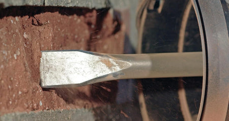 Extreme close-up of the Bosch 10-inch SDS-Plus heavy-duty alloy steel chisel bit penetrating and shattering red masonry brick.