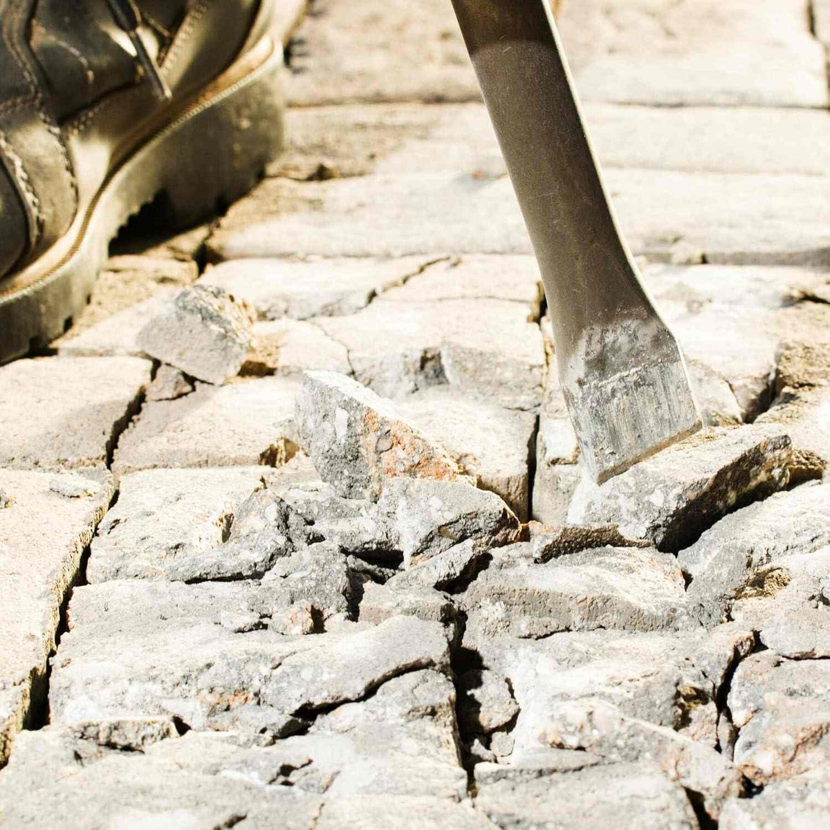 Bosch SDS-Plus Bulldog hammer steel chisel bit actively breaking up concrete pavers on the ground beside a construction worker's boot.