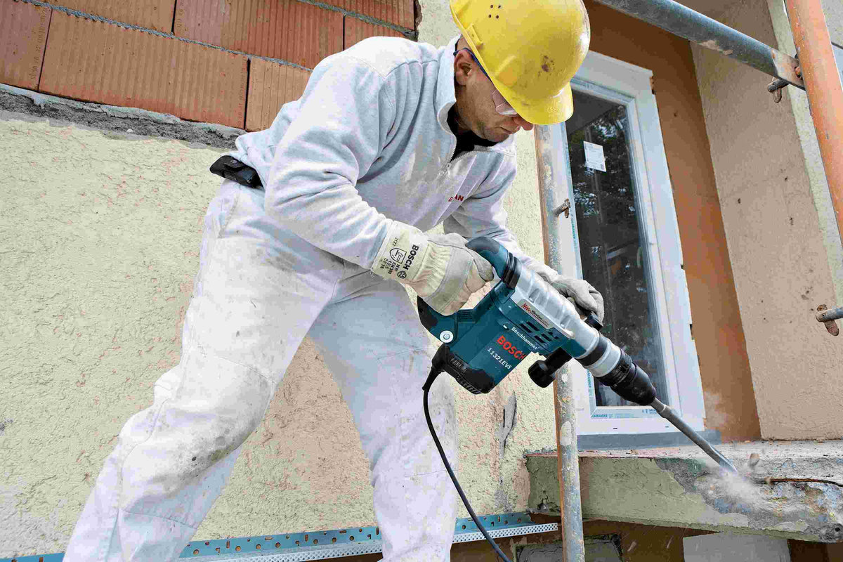 An action shot of a construction worker using a Bosch rotary hammer with the HS1465 tile chisel to break up a concrete ledge on an outdoor jobsite.