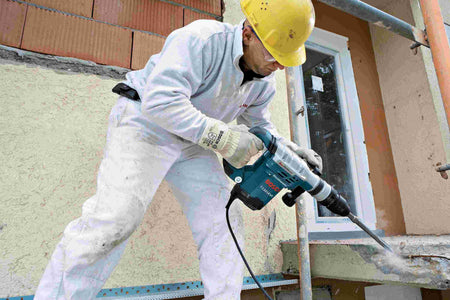 An action shot of a construction worker using a Bosch rotary hammer with the HS1465 tile chisel to break up a concrete ledge on an outdoor jobsite.