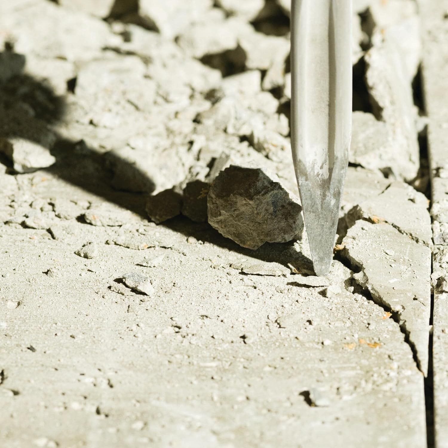 Close up high angle field shot of the star point tip profile on a Bosch self sharpening twist chisel bit initiating a stress line fracture crack inside a weathered concrete slab surface background.