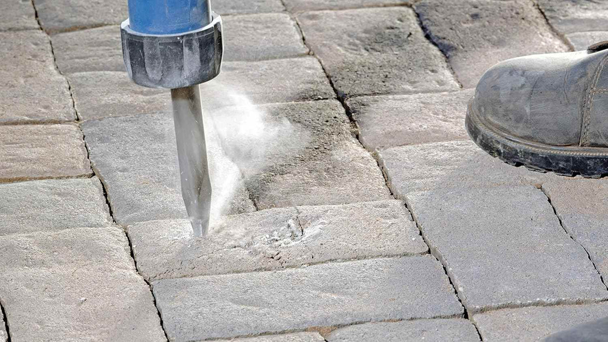 An application shot of the Bosch 16-inch bull point chisel breaking up stone pavers, showcasing the tool's precision and power in heavy-duty outdoor demolition environments.