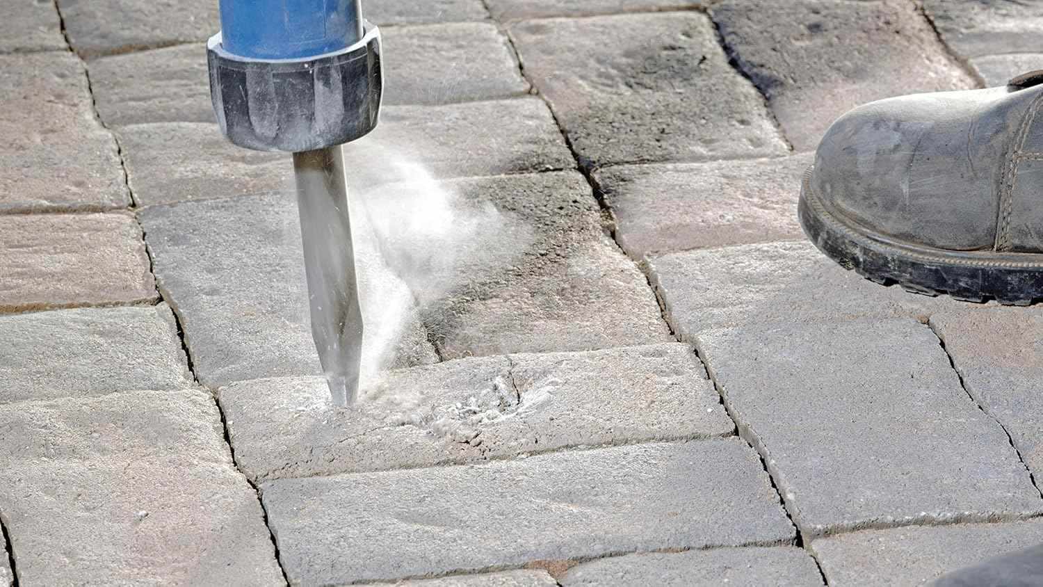 An application shot of the Bosch 16-inch bull point chisel breaking up stone pavers, showcasing the tool's precision and power in heavy-duty outdoor demolition environments.