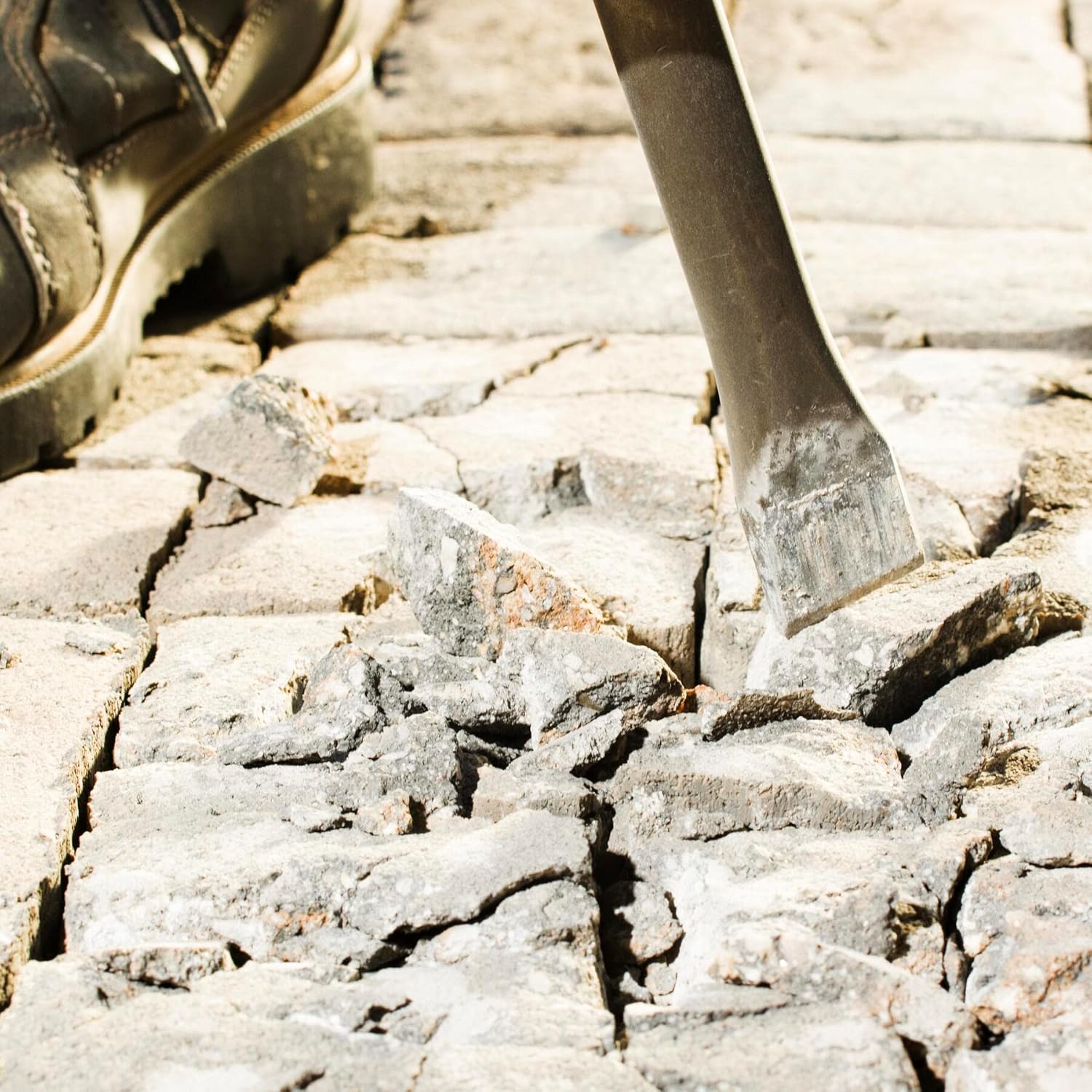 An action view of a worker using the flat chisel bit to shatter and fracture concrete paver stones on a jobsite floor, with fractured stone fragments scattered around the impact zone.