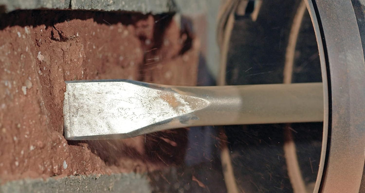 A macro close-up view of the flat chisel head of the Bosch HS1911 masonry bit breaking into a red brick mortar joint, demonstrating precise directional chipping and channeling.