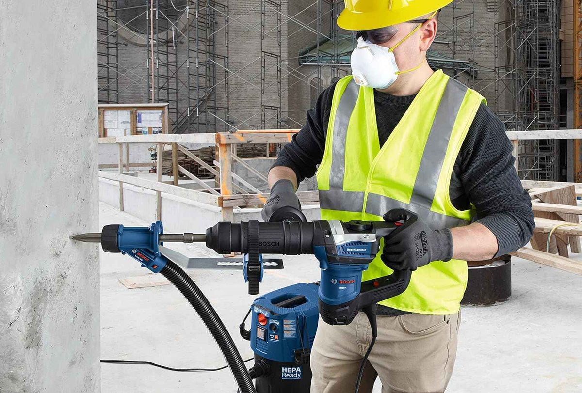 An action shot of a professional contractor in safety gear using a Bosch SDS-max rotary hammer equipped with the HS1934 star point chisel and a dust extraction system to demolish a concrete wall on a jobsite.